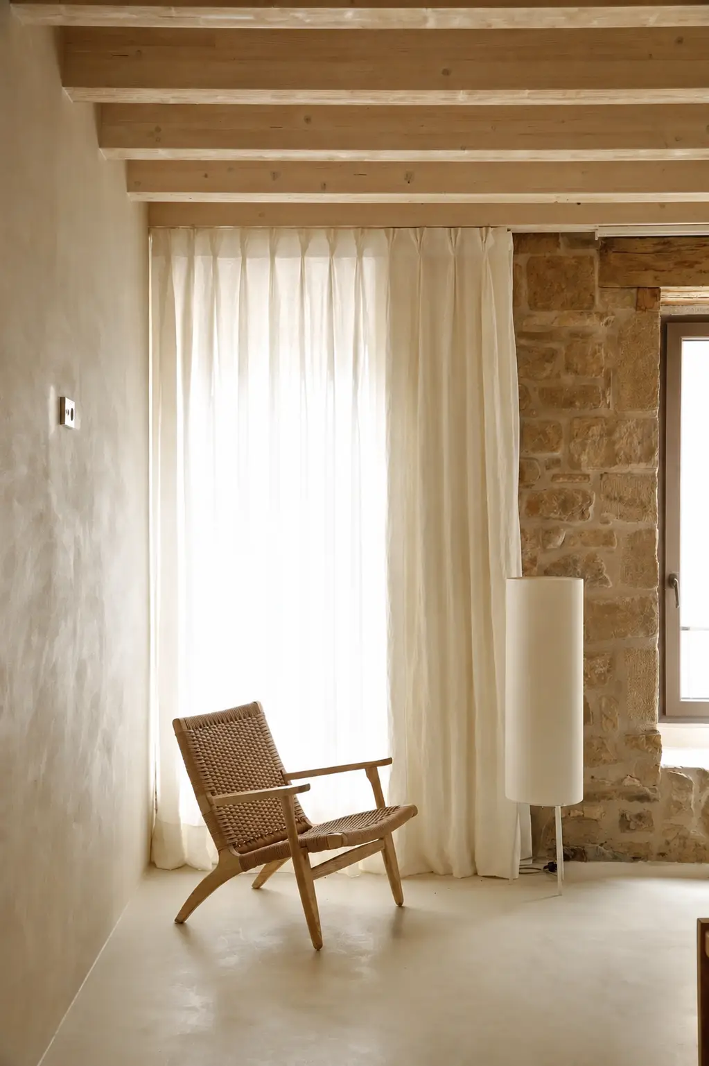 Interior rústico contemporáneo con suelo y pared revestidos con acabado continuo MicroQuarz®, vigas de madera y muro de piedra.